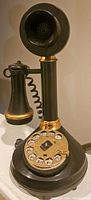 Front angle of the telephone showing the black body, gold accents, and rotary dial with letters and numbers.
