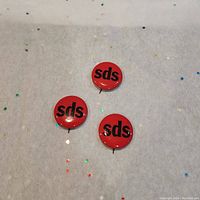 Front view of three red 1960s SDS political buttons with black 'sds' text.