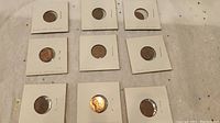 All nine US pennies placed in protective holders laid out on fabric surface.