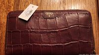 Front exterior view of brown croc-embossed leather Fossil wallet with attached tag and gold tone logo plaque.