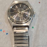 Silver-tone men's Bulova Accutron wristwatch with black dial and silver hour markers and hands. Metal link band shown. Watch face shows wear and scratches.