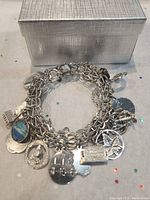 Photo of the silver charm bracelet with multiple charms including a maple leaf in circle, hotel key fob, and Thunder Bay enamel charm.