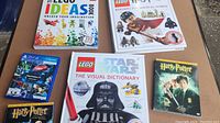 Lot of children's LEGO books, LEGO Star Wars visual dictionary, LEGO Harry Potter book, Harry Potter DVDs, and a PS4 game placed on a brown surface.