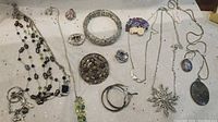 Photo of various pieces of costume jewelry displayed on a white surface including necklaces, bracelets, brooches, rings, and earrings.
