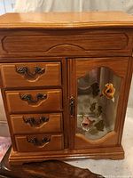 Medium brown wooden jewelry box with four drawers and a glass door with floral decoration.