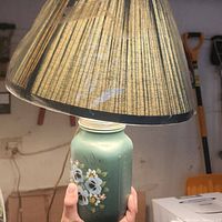 Photo of the green pansy floral lamp with beige pleated shade held by hand.