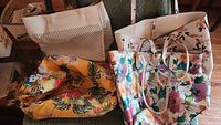 Four spring/summer purses on a chair including one cream perforated, two floral pattern purses, and a yellow floral purse with strap.
