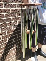Wind chime held up showing metal tubes and wooden frame with cord for hanging.