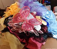 Pile of assorted dress-up fabric pieces and pink butterfly wings accessory spread out on surface