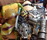 Ninja Turtles costume and various Transformers costume parts including helmets and limb armor pieces laid out on a surface
