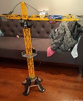 Full view of the large remote control crane toy set up on floor in front of couch. Shows the yellow lattice crane tower with black and red base supports.