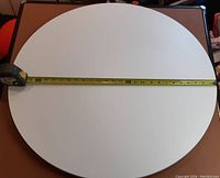 Top view of a white round lazy Susan with measuring tape crossing it horizontally showing the diameter
