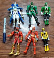 Group of six Power Rangers action figures on wood floor with blue Sharpie marker for scale