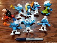 Photo of all nine figurines from above with a pen for scale on a wood floor.