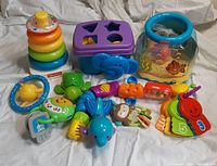 Full lot of assorted Fisher Price baby toys displayed on white fabric background, showing various colorful plastic infant toys including stackable rings, shape sorter, and key toys.