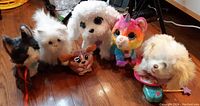 Five assorted FurReal electronic toys arranged on wooden floor, showing variety of species and colors including unicorn, dogs, and small creature.