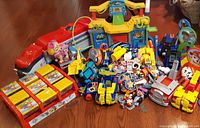 Overview photo of assorted Paw Patrol toys including vehicles, characters, and playsets on wooden floor