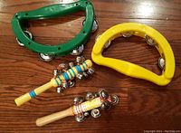 Green and yellow half moon tambourines with two colorful wooden jingle sticks on a wooden floor