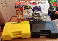 Photo of boxed K'NEX Super Mario 3D Land Ghost House set with two plastic K'NEX carrying cases (yellow and black) in front.