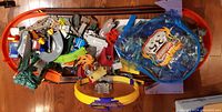 Large pile of mixed Hot Wheels track accessories including orange track pieces, curved and straight sections, connectors in various colors and some small parts in plastic bag with Hot Wheels logo