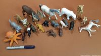 Wide shot of the lot of assorted plastic animal figurines including large and small animals, with a Sharpie pen for scale.