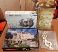 Four main boxed items: Marble Night City kit, DaVinci's Secret Cube box, Kodacolor 750-piece castle puzzle box, plus loose marble run parts in plastic bag on table