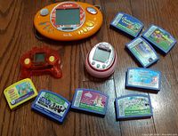 Lot overview showing all items together on a wooden floor, including VTech Quiz Biz, Tamagotchi Friends, red translucent game device, and nine Leapster cartridges