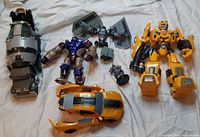 Lot of assorted Transformers figures including Bumblebee, Devastator Cement Mixer Truck, Optimus Primal Maximal, and Star Wars crossover Tie Pilot and Tie Bomber in robot and vehicle modes on white fabric background.