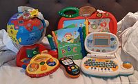 Photo showing entire lot including Play & Learn Globe, Lil' SmartTop electronic laptop, Click and Count Remote, Touch and Teach Busy Books with interactive learning books, and other assorted toddler toys.