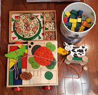 Top view of lot showing wooden pizza puzzle, bucket of multicolor blocks, pull cow toy, and pull cart with ladybug.
