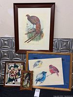 Four framed art pieces arranged in a group including the large pheasant print, three bird paintings on blue background, stained glass floral art, and small carved wooden framed bird illustration.