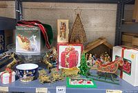 Shelf with various Christmas decorations including metal reindeer, crystal deer in silk sleigh, wrapped gift ornaments, decorative bowls, rustic metal tree with star topper, painted wooden sleigh, and nativity stable.