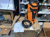 Overview of Deco Home 1800W power washer unit standing on its box with attached power cord, hose and spray wand laid beside it along with instruction manual visible.