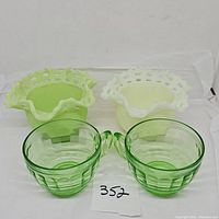 Top-down view of two mustard yellow glass bowls with basket weave pattern and two green uranium glass cups, placed on white cloth background