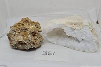 Two geodes shown side by side on a white backdrop with a lot number card '361'. One is a large clear white quartz geode showing a hollow crystalline interior, the other is a rough mineral rock.