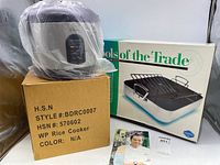 Wolfgang Puck rice cooker on top of its box, adjacent to the Tools of the Trade roasting pan box with printed brand and picture of pan with rack.