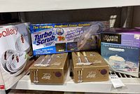 Photo showing Turbo Scrub 360 cordless handheld power scrubber box, Wheeler & Worth porcelain tea kettle box, and two boxes of Cristal 2000 stemware glasses.