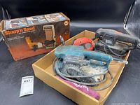 Lot showing the Makita belt sander, Black & Decker palm sander, and boxed drill-powered belt sander