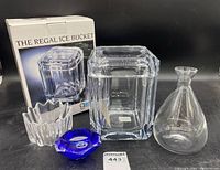 Photo showing the clear Lucite Regal ice bucket with original box, clear signed decanter, and two glass candle holders (one clear, one blue).