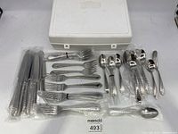 Full view of all flatware pieces including knives, forks, spoons and serving utensils with a white plastic storage box.