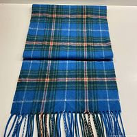Folded blue and green tartan wool scarf laid flat to show pattern and fringed ends