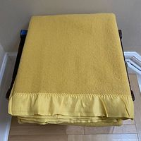 Top view of folded mustard yellow wool blanket showing satin binding edge