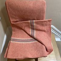 Full view of wool blanket draped over a chair showing its muted tangerine color and stripes on the ends.