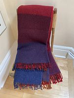 Blanket neatly folded on a wooden chair with visible fringe detail and rich color blocks of burgundy and blue.