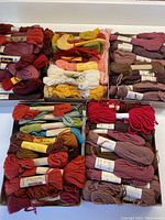Boxed skeins of wool tapestry yarn in deep reds, purples, and browns.