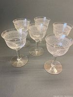 Six etched crystal aperitif/liqueur glasses arranged in a group on a gray surface.