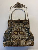 Front view of the rectangular beaded evening bag with metal curved handle and attached chain