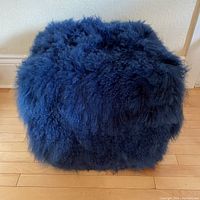 Sheepskin foot rest from front angle showing thick dark blue wool covering and square shape.