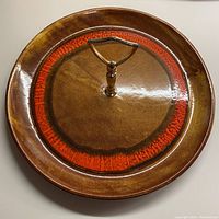 Top view of round serving plate showing the cinnamon brown background with burnt orange ring and brass handle in the center.