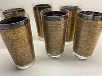 Angle showing all six glass tumblers standing upright, showcasing the full set and their gold wire-style exterior decoration.